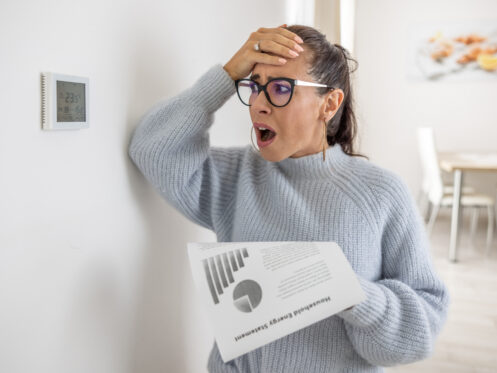 High heating bill homeowner looking at thermostat